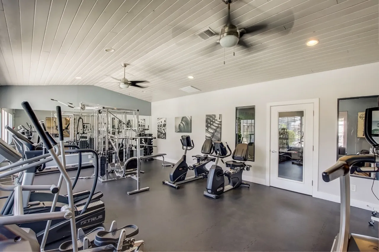 Fitness center, exercise equipment, dark flooring, ceiling fans, mirrors