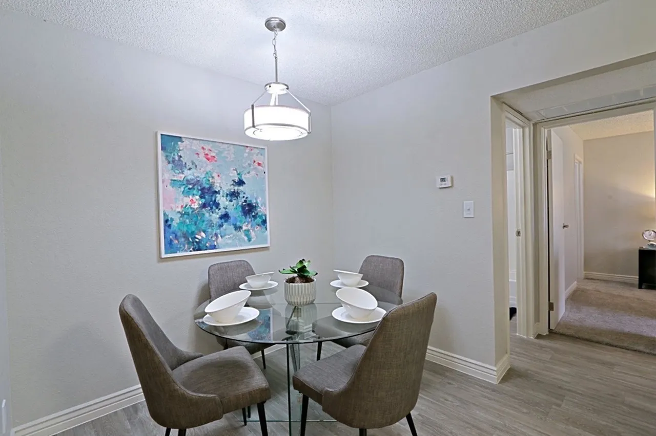 Dining room with round glass table, gray upholstered chairs, pendant lighting, wood-style plank flooring