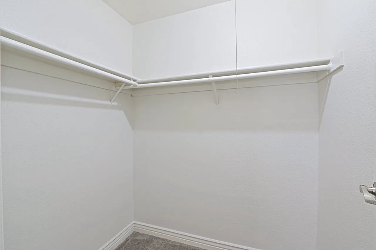 Empty walk-in closet, metal hanging rods, white walls, concrete flooring