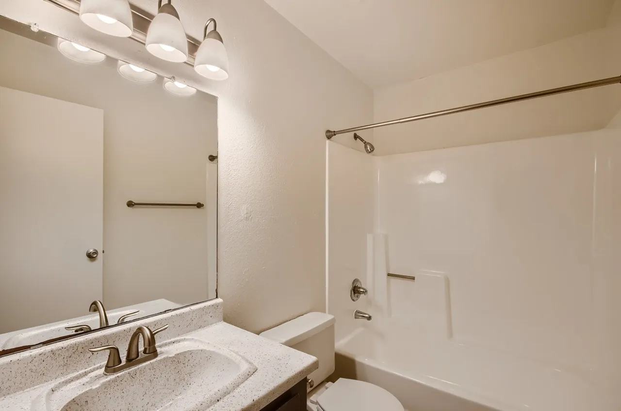 Primary bathroom, dual vanity with stone countertops, framed mirror, bronze fixtures, soaking tub with glass enclosure