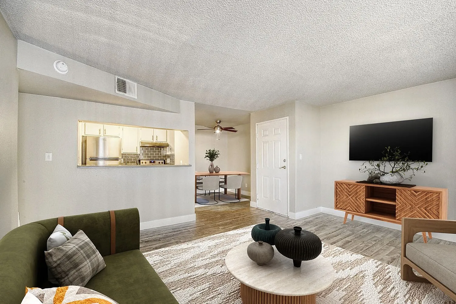 Living room with olive green sofa, wood-style plank flooring, ceiling fan, mounted TV above wooden media console