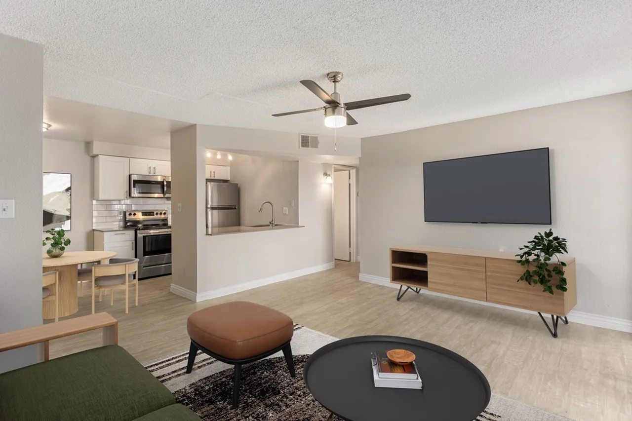 Living room with wood-style plank flooring, ceiling fan, wall-mounted TV, open kitchen with stainless appliances