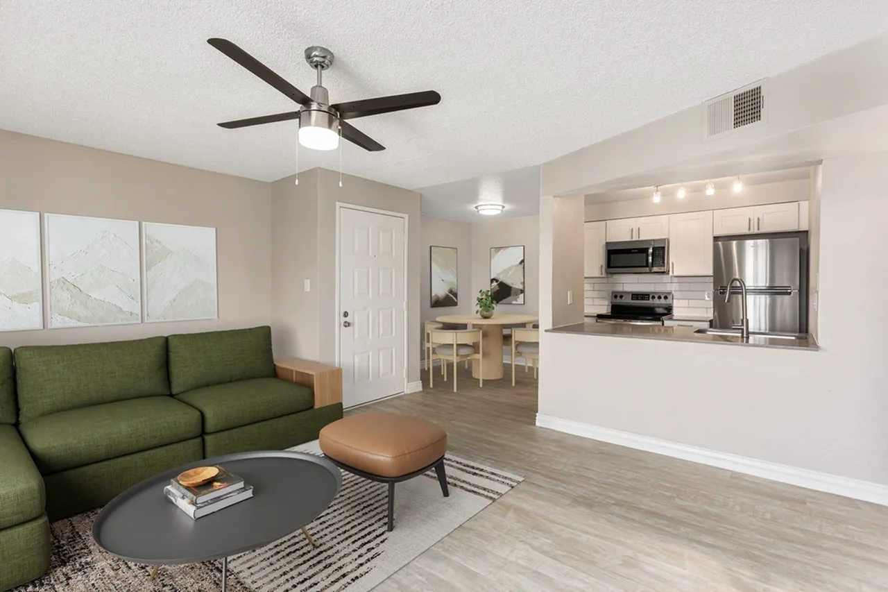Living room with green sofa, wood-style plank flooring, ceiling fan, open kitchen with stainless appliances