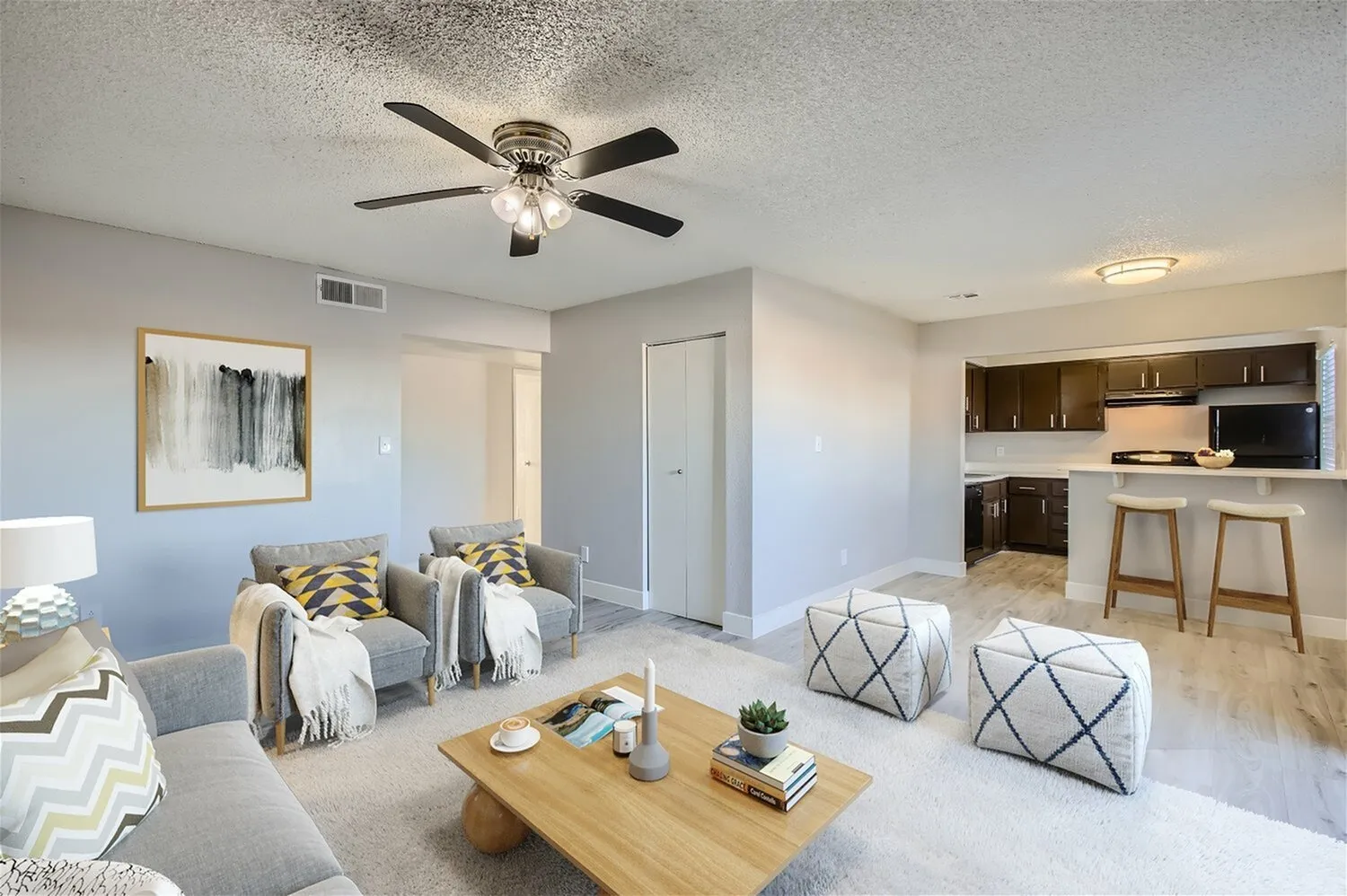 Living room with wood-style plank flooring, ceiling fan, dark wood cabinetry, breakfast bar