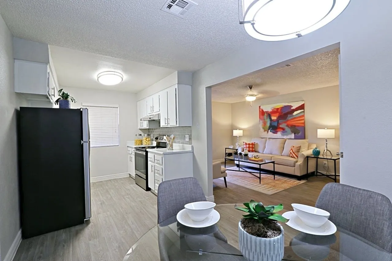 Dining area with table and chairs, kitchen with white cabinetry and stainless appliances, wood-style plank flooring