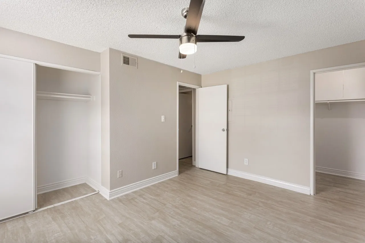 Primary bedroom, wood-style plank flooring, ceiling fan, multiple closets