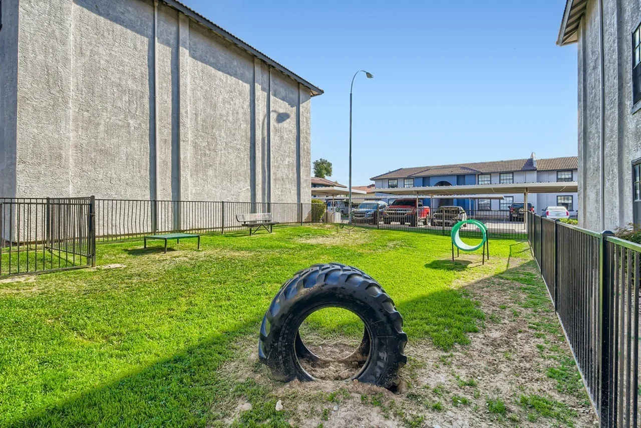 Outdoor play area, tire obstacle, green grass, metal fencing, residential buildings