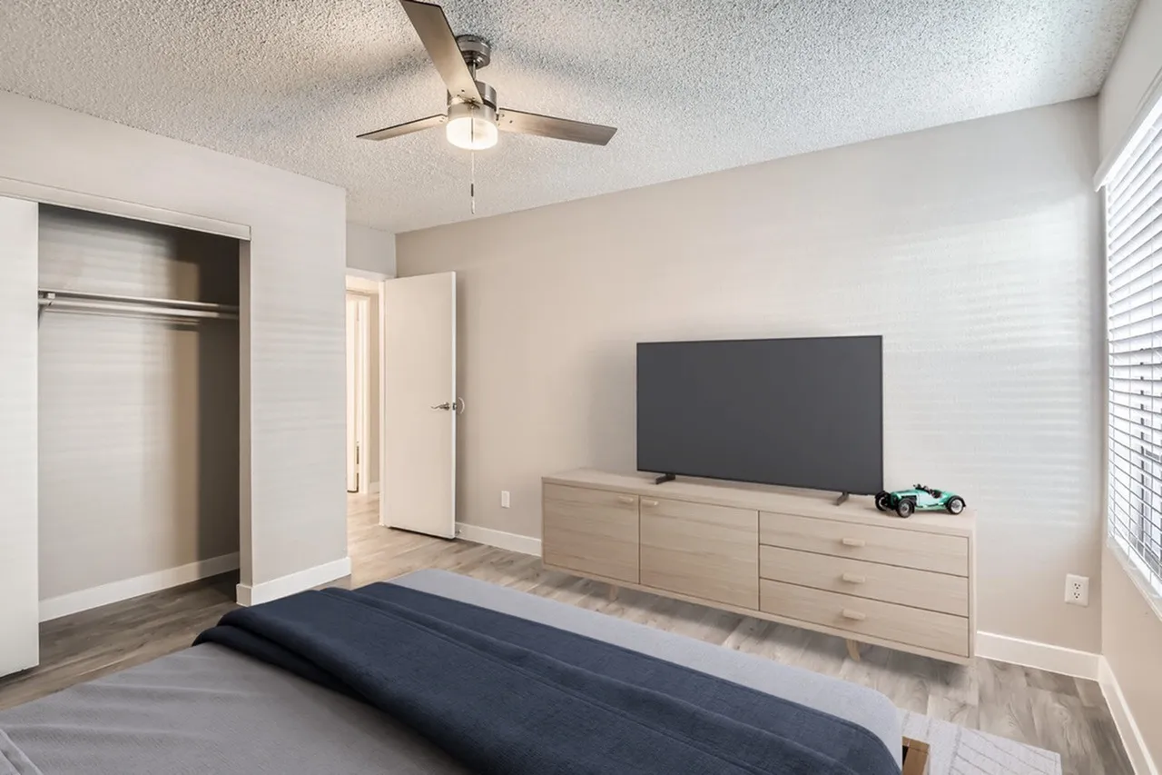 Primary bedroom, wood-style plank flooring, ceiling fan, media console with television