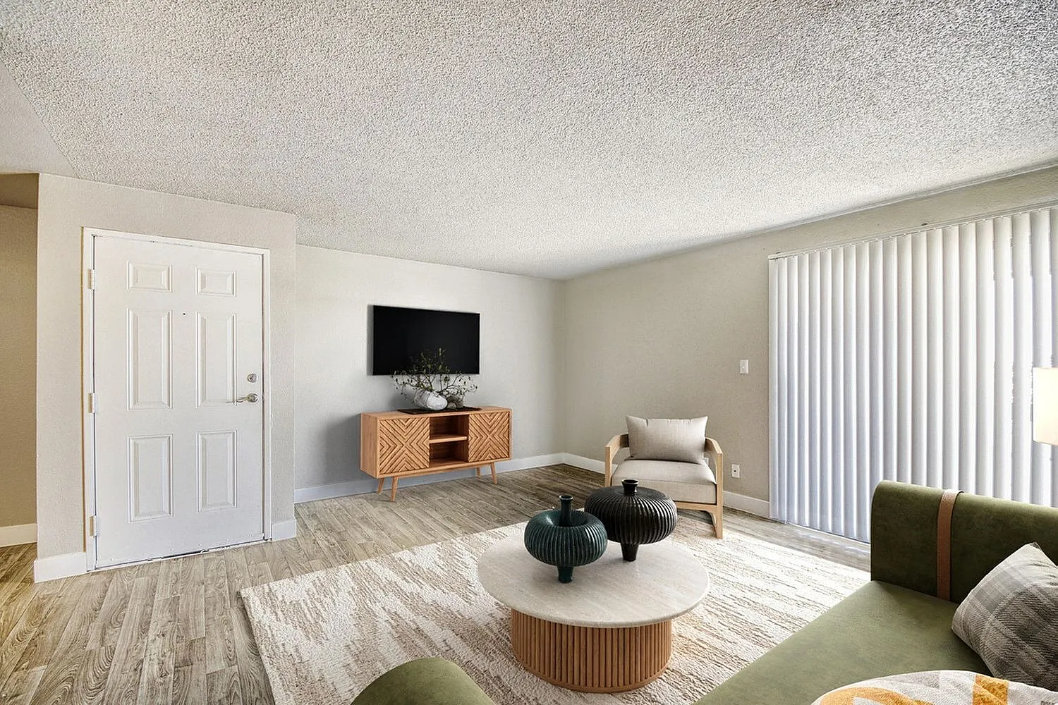 Living room, wood-style plank flooring, round white coffee table, flat screen TV, vertical blinds