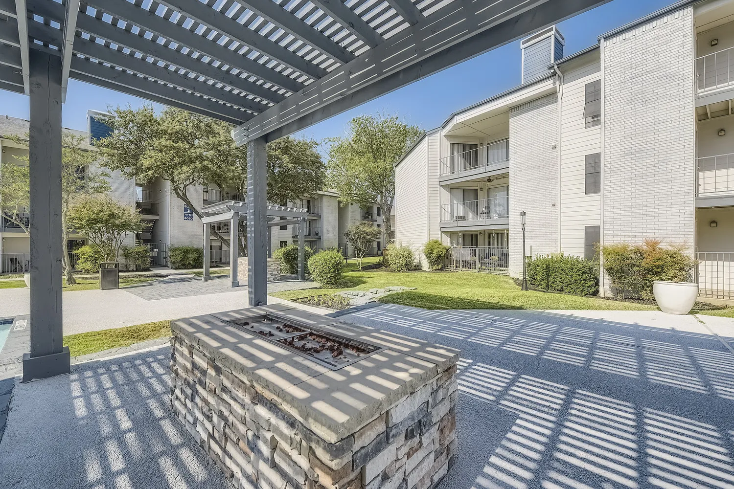 Outdoor fire pit lounge area under a pergola near the pool
