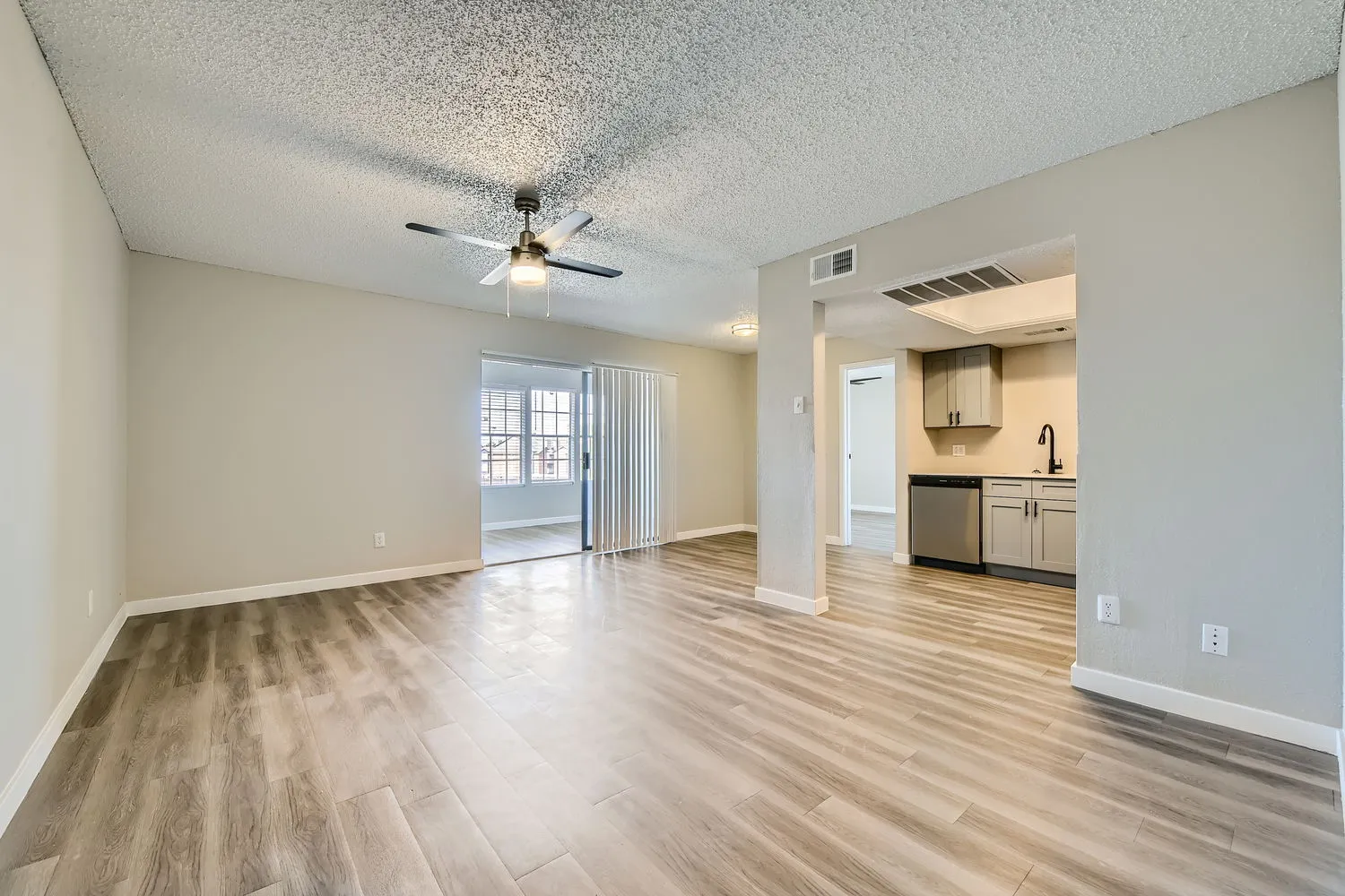 Living room with wood-style plank flooring, ceiling fan, sliding glass door to sunroom, pass-through view to kitchen
