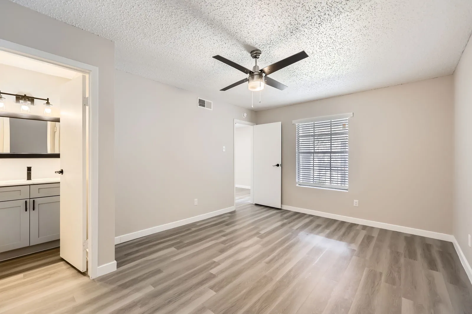 Primary bedroom with wood-style plank flooring, ceiling fan, en-suite bathroom entry, window