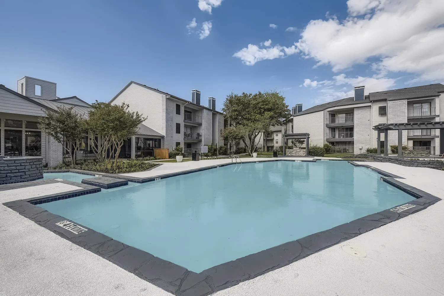 Community pool with sun deck, surrounded by landscaping and residential buildings