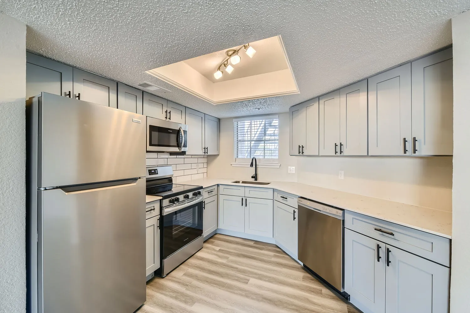 Kitchen with gray shaker cabinets, quartz countertops, subway tile backsplash, stainless steel appliances
