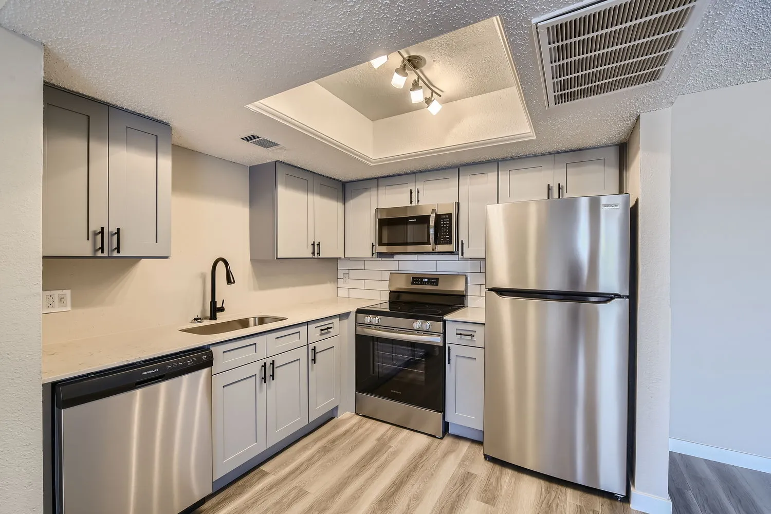 Kitchen with gray shaker cabinets, quartz countertops, subway tile backsplash, stainless steel refrigerator, range, and dishwasher
