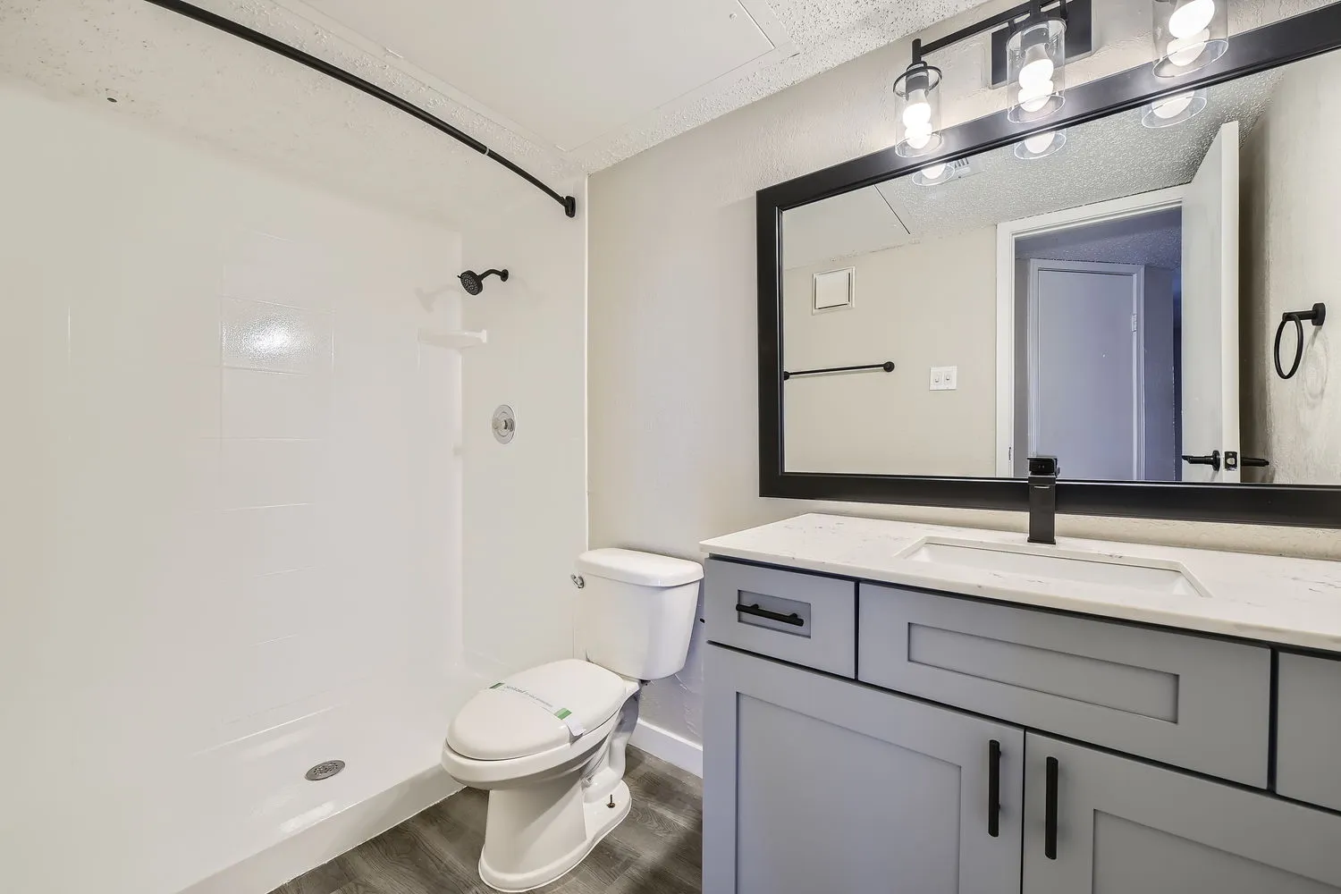 Primary bathroom with quartz vanity countertop, matte black fixtures, framed mirror, walk-in shower
