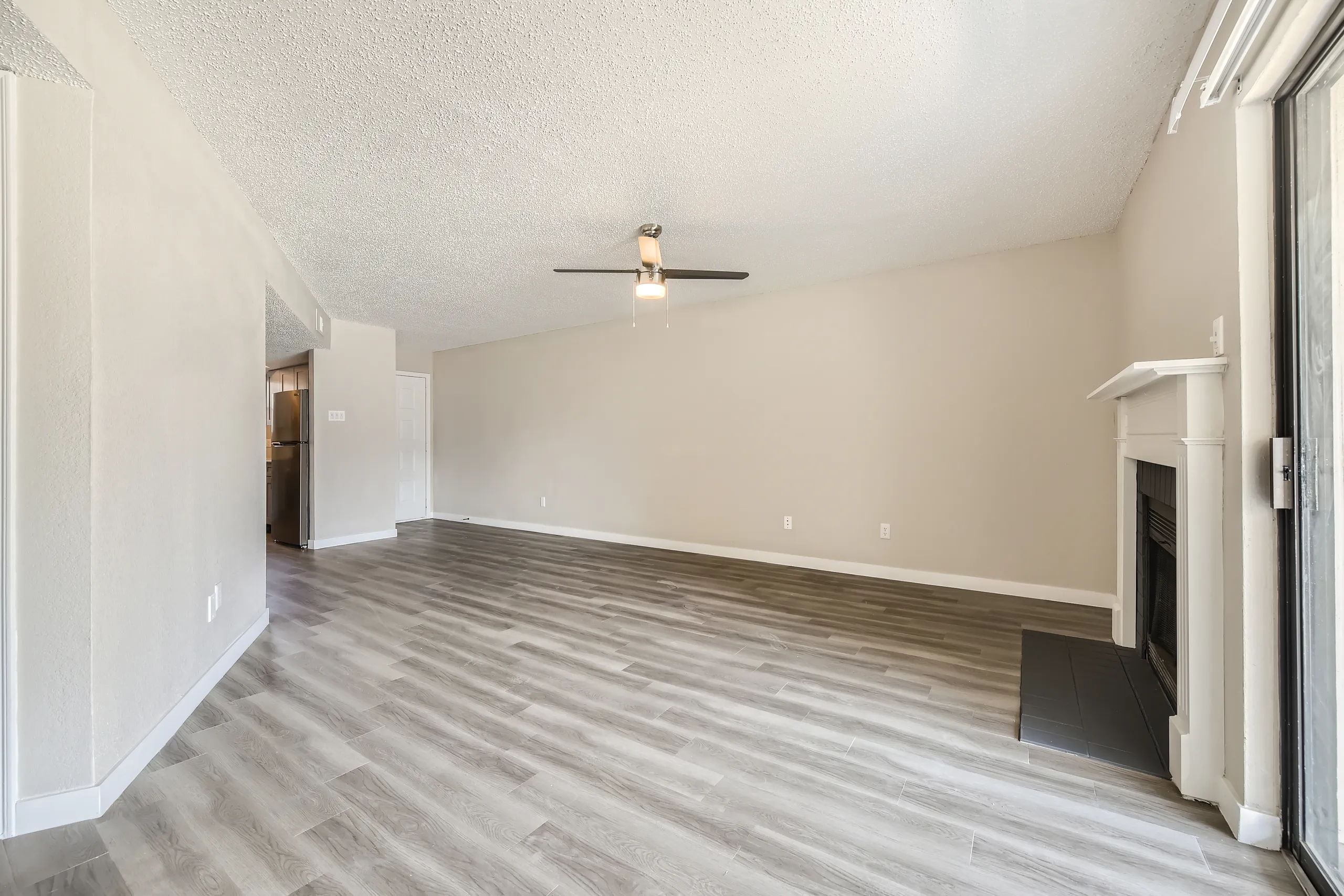 Living room with wood-style plank flooring, ceiling fan, fireplace, view into kitchen