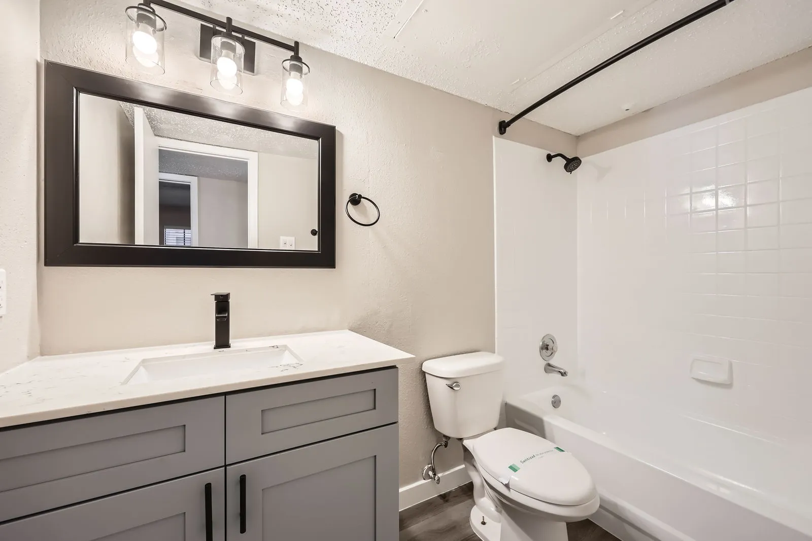 Bathroom with quartz vanity countertop, matte black fixtures, framed mirror, tub-shower combo