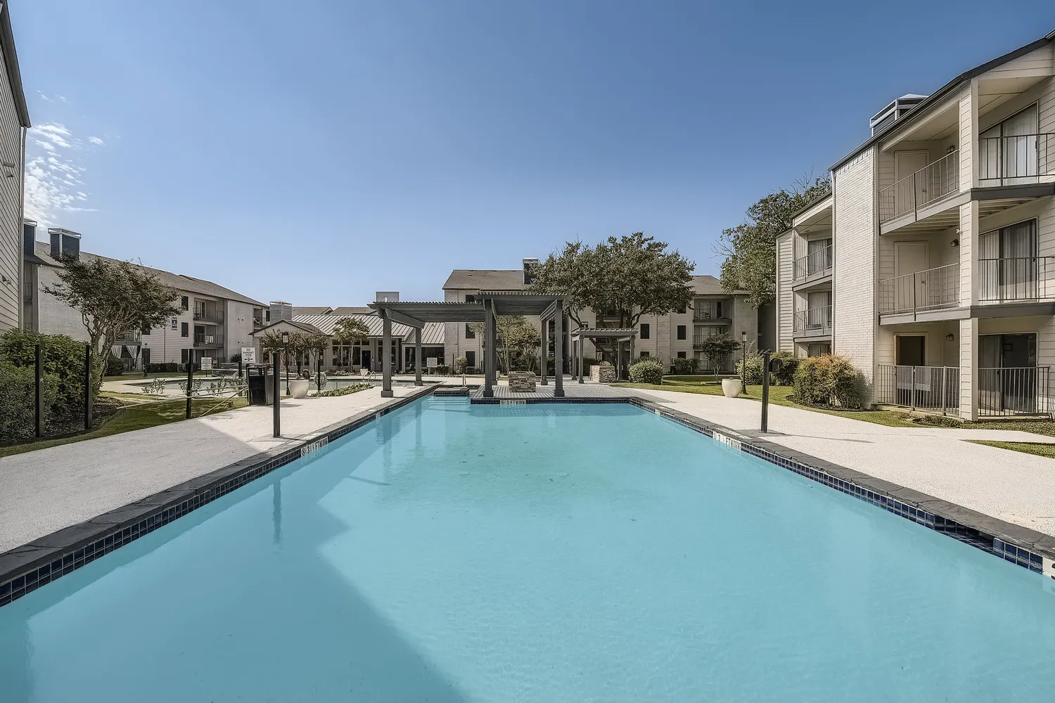 Community pool with sun deck and pergola, view toward residential buildings