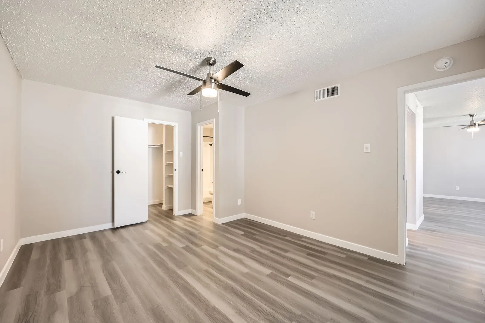 Primary bedroom with wood-style plank flooring, ceiling fan, walk-in closet, en-suite bathroom entry