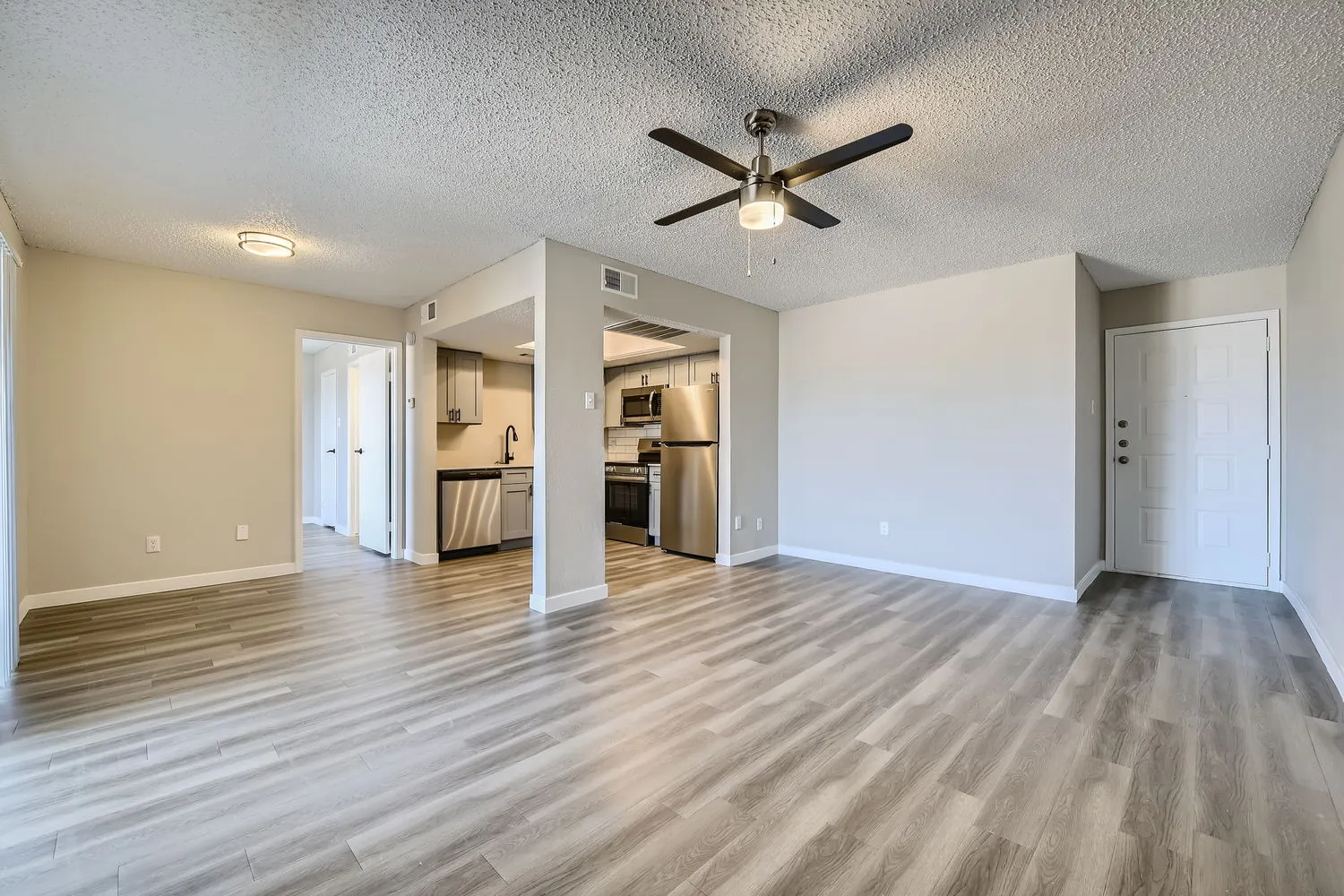 A5 Platinum floor plan, open living room with wood-style plank flooring, ceiling fan, view into kitchen with stainless steel appliances