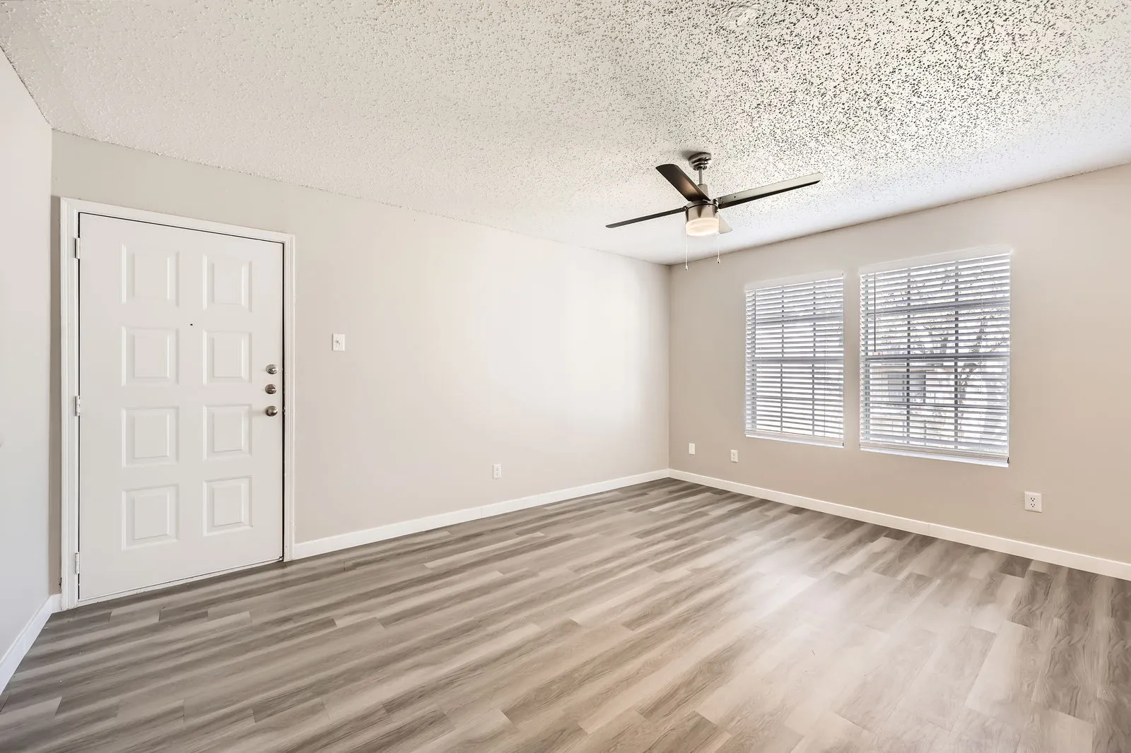 Living room with wood-style plank flooring, ceiling fan, entry door, large windows with natural light