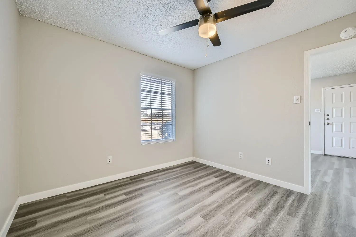 Primary bedroom, ceiling fan, entry door view, wood-style plank flooring