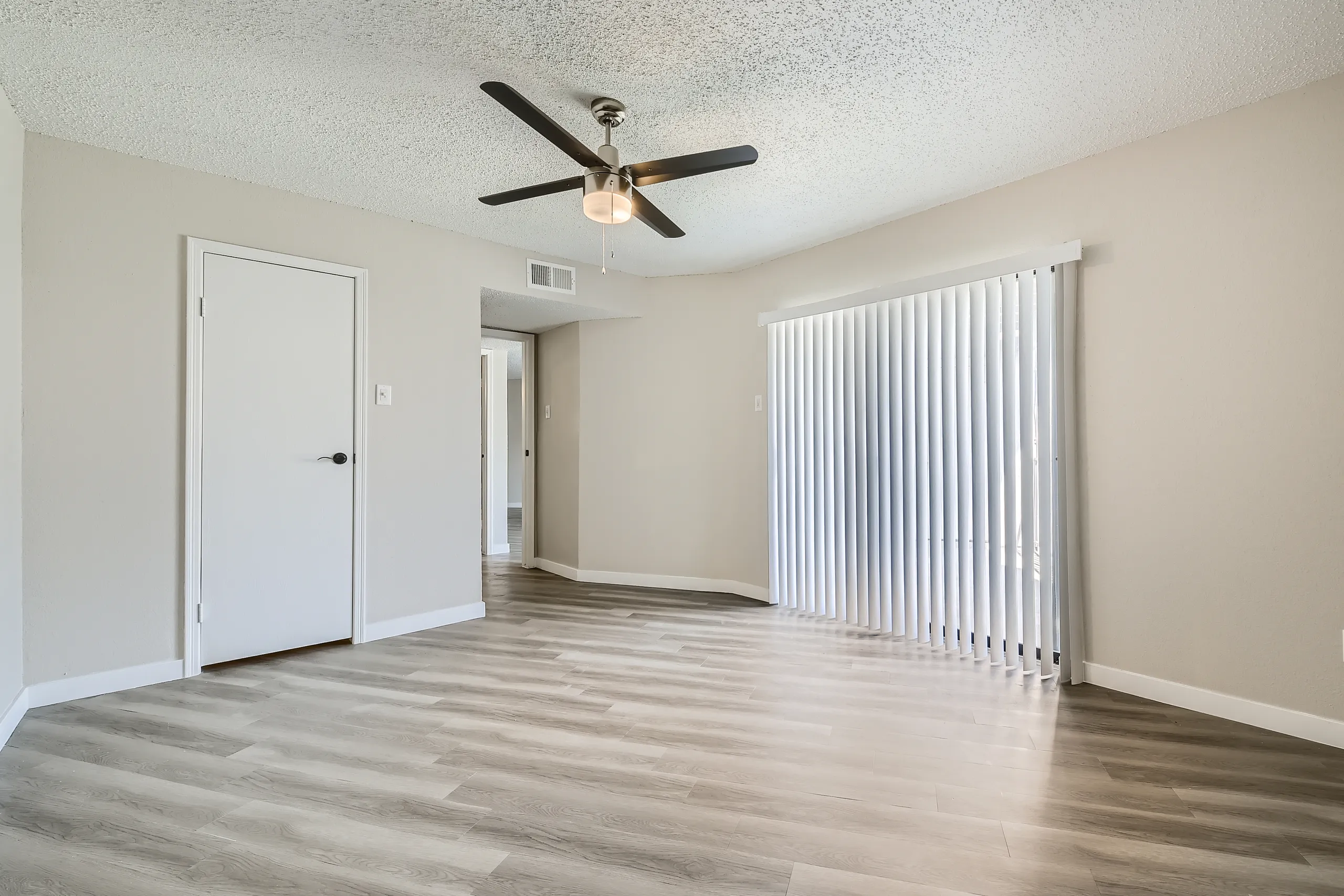 Primary bedroom with wood-style plank flooring, ceiling fan, closet door, hallway view
