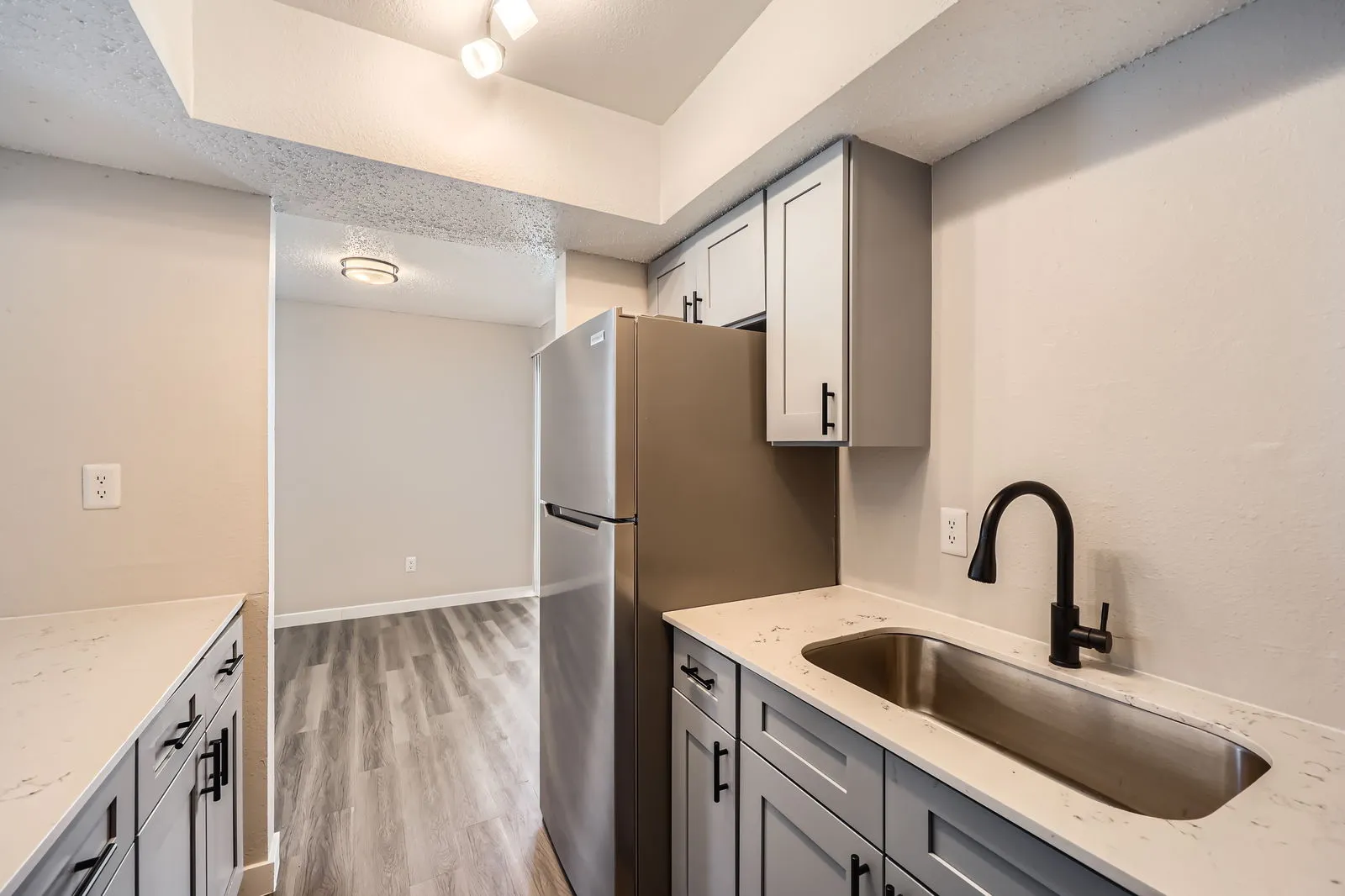 Kitchen with gray shaker cabinets, quartz countertops, stainless steel refrigerator, view into dining area