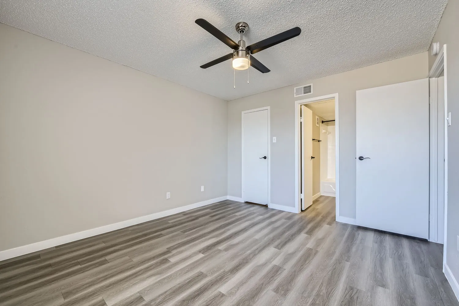 Bedroom with wood-style plank flooring, ceiling fan, two closet doors, en-suite bathroom entry