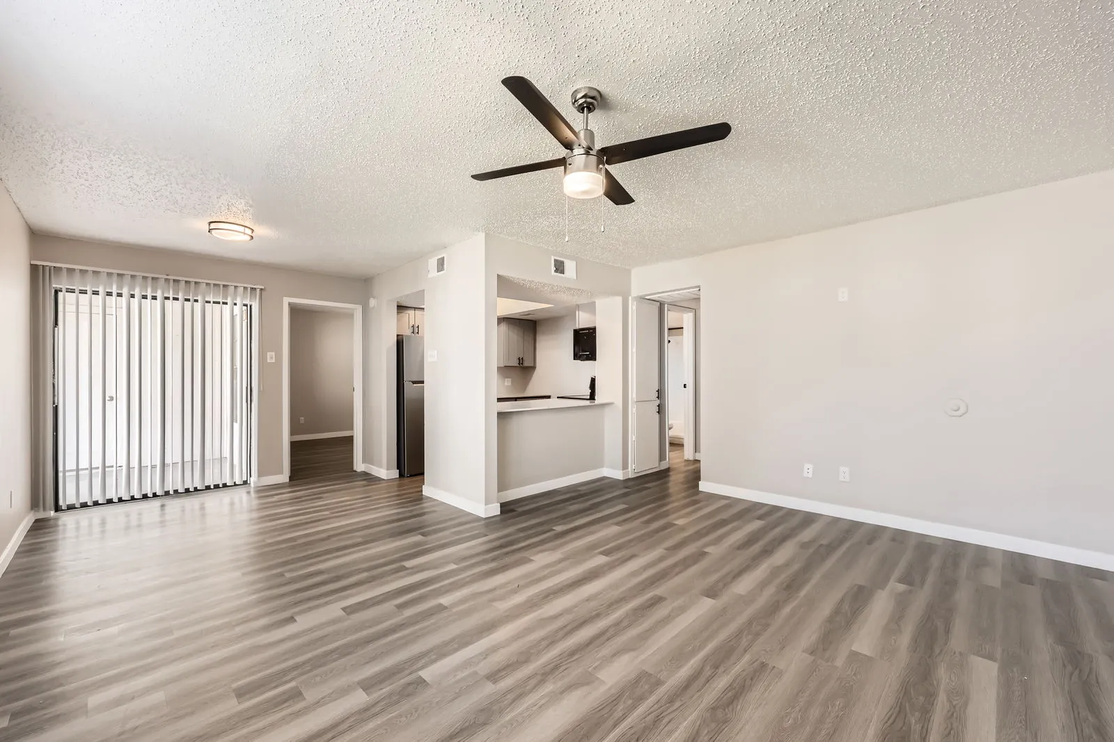 B1 Platinum floor plan, open living room with wood-style plank flooring, ceiling fan, sliding glass door, pass-through view to kitchen