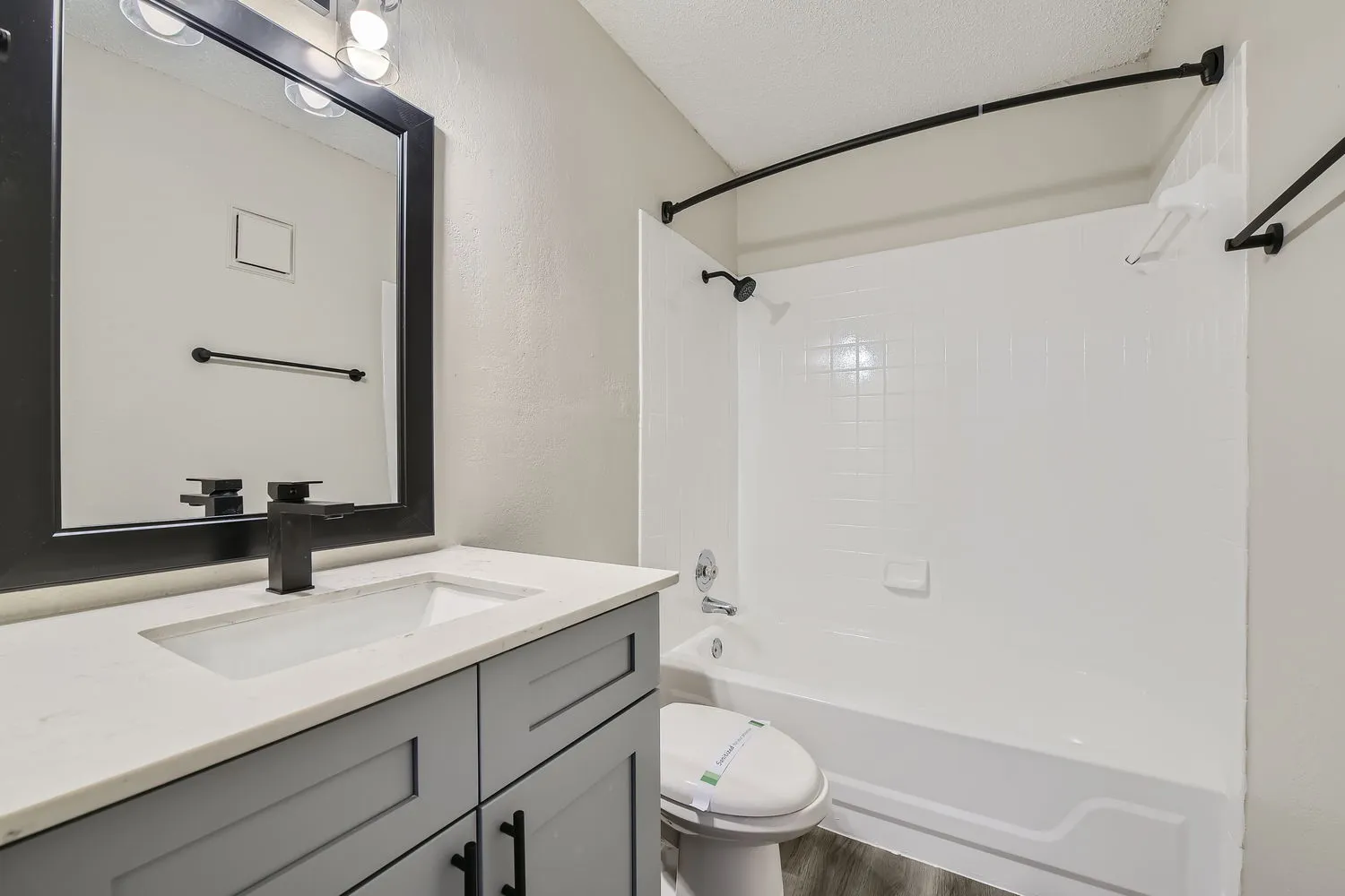 Bathroom with quartz vanity countertop, matte black fixtures, framed mirror, tub-shower combo