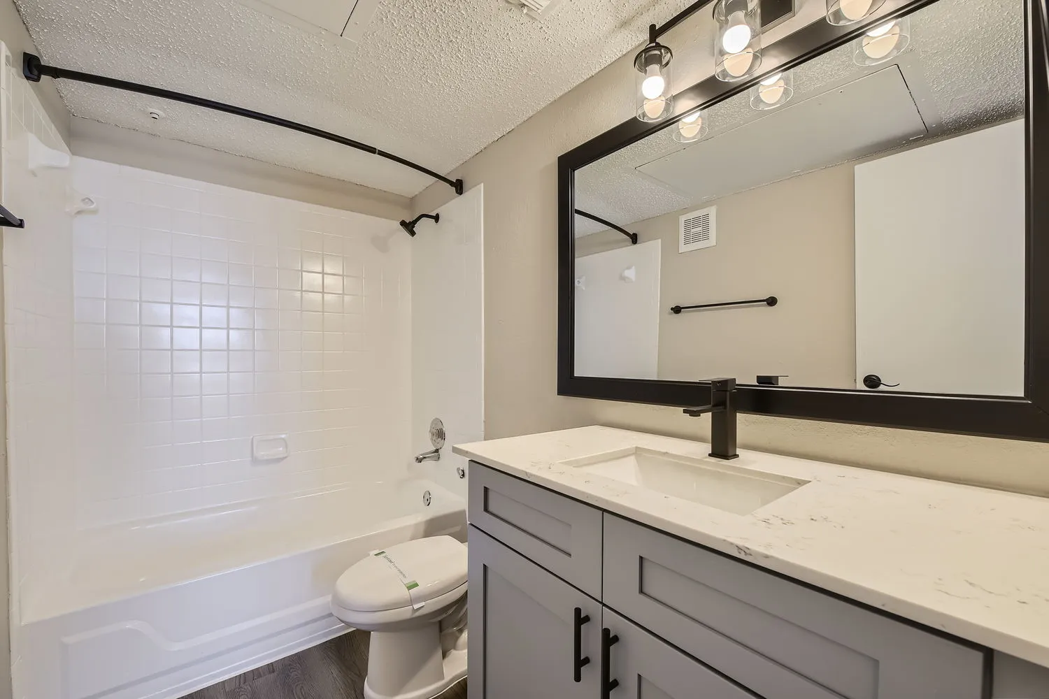 Bathroom with quartz vanity countertop, undermount sink, matte black fixtures, framed mirror, tub-shower combo