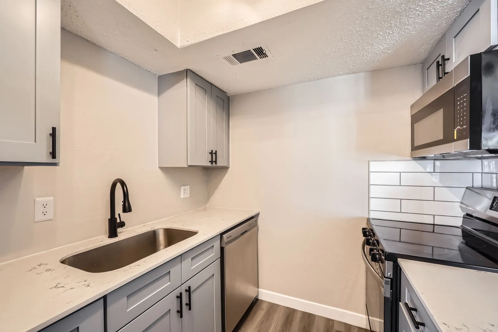 Kitchen with gray shaker cabinets, quartz countertops, subway tile backsplash, stainless steel appliances