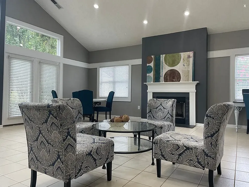 Living room, patterned wingback chairs, fireplace with white mantel, wood-style plank flooring, dark gray accent wall