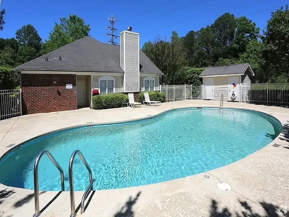 Resort-style pool, concrete deck, black metal railings, brick clubhouse, manicured landscaping, blue sky