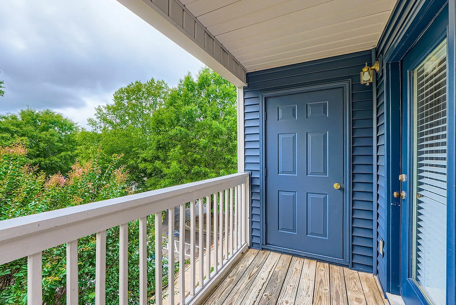 Front porch with white railing, blue entry door, wood-style plank flooring, blue siding