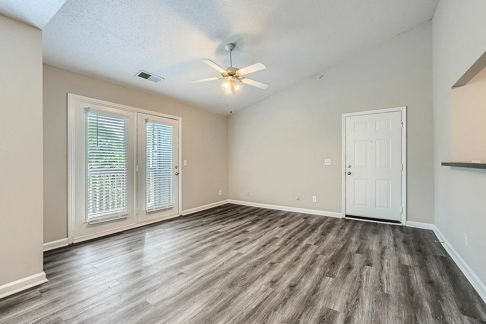 Living room, wood-style plank flooring, ceiling fan, glass sliding doors, entry door