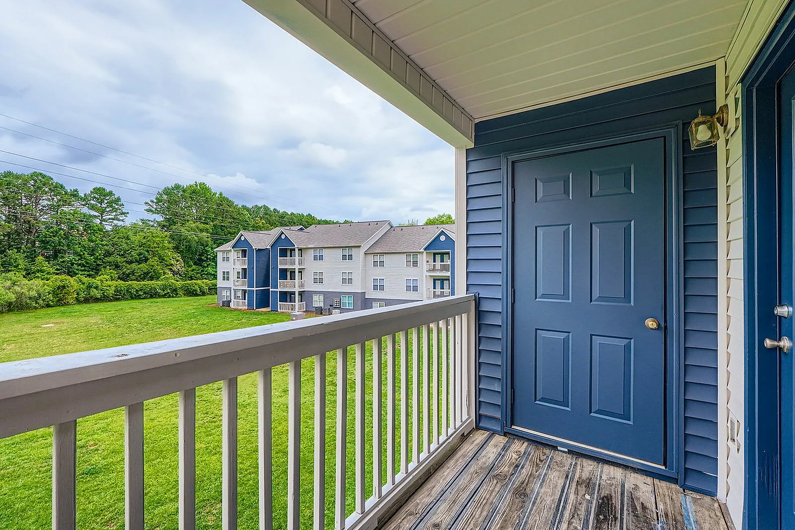 Covered balcony, white railing, dark blue entry door, wood-style plank flooring
