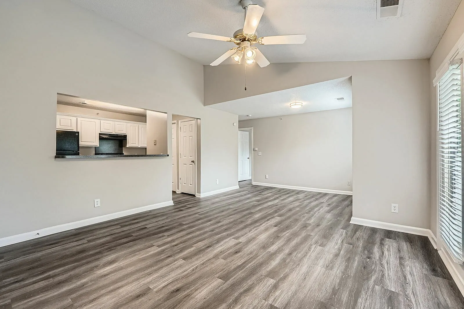 Living area with wood-style plank flooring, ceiling fan, cream cabinetry, entry hallway
