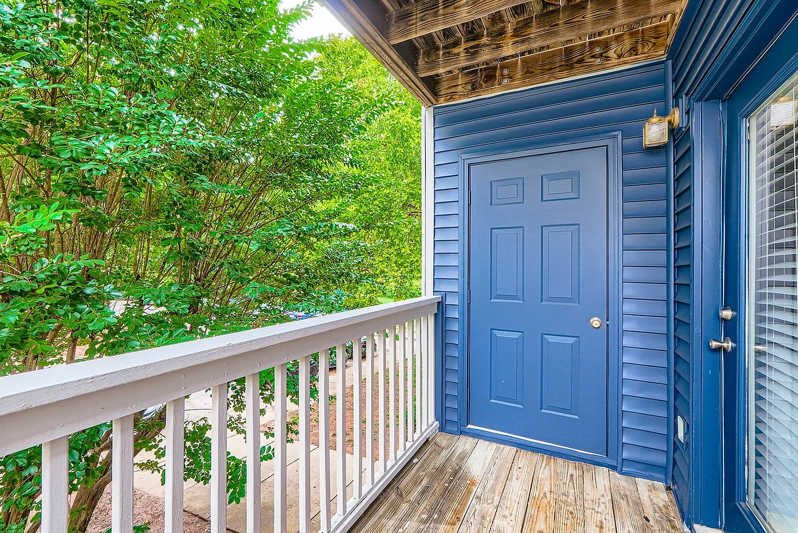 Front porch, blue door, white railing, wood-style plank flooring, green foliage