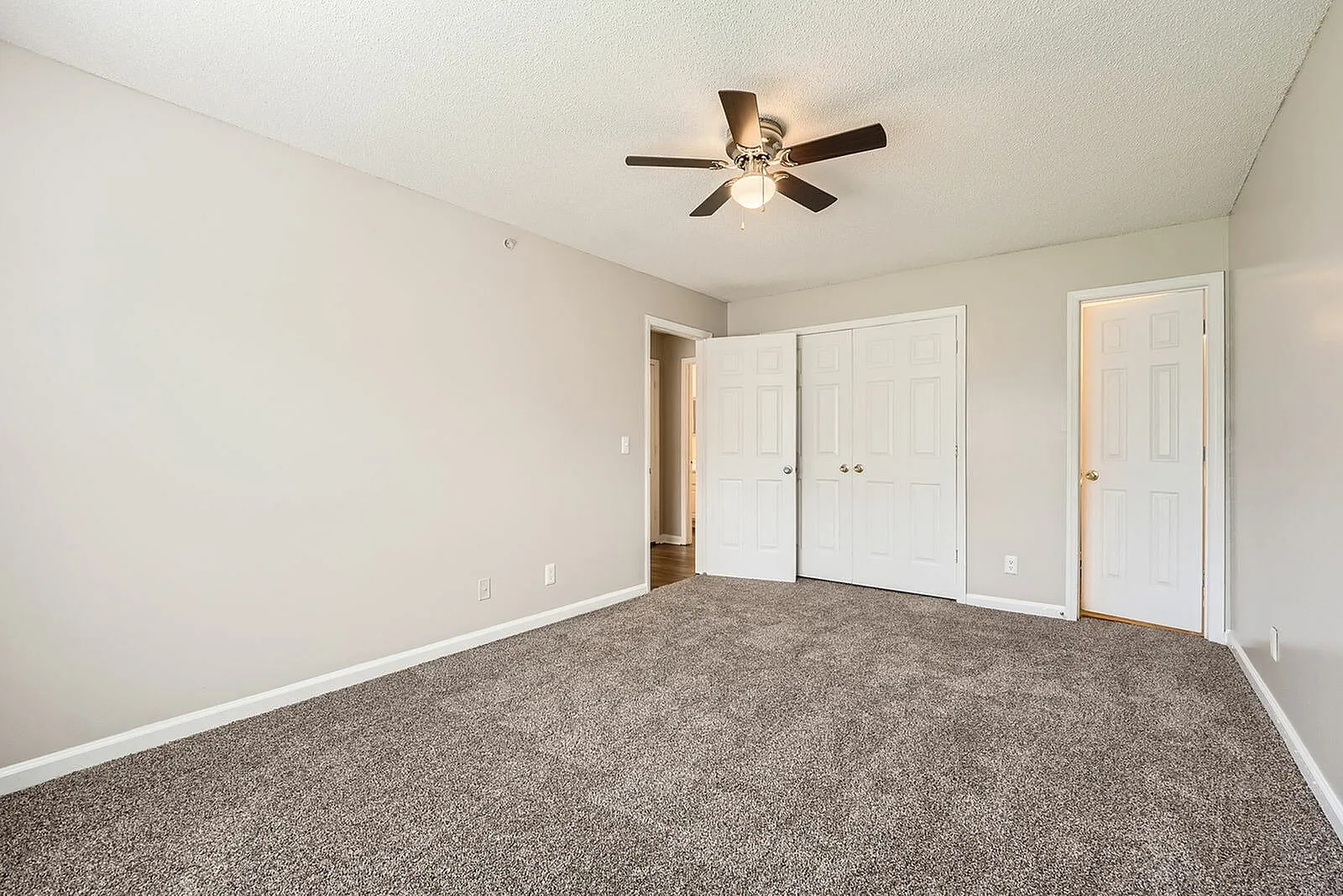Bedroom, gray carpet flooring, white closet doors, ceiling fan with light fixture