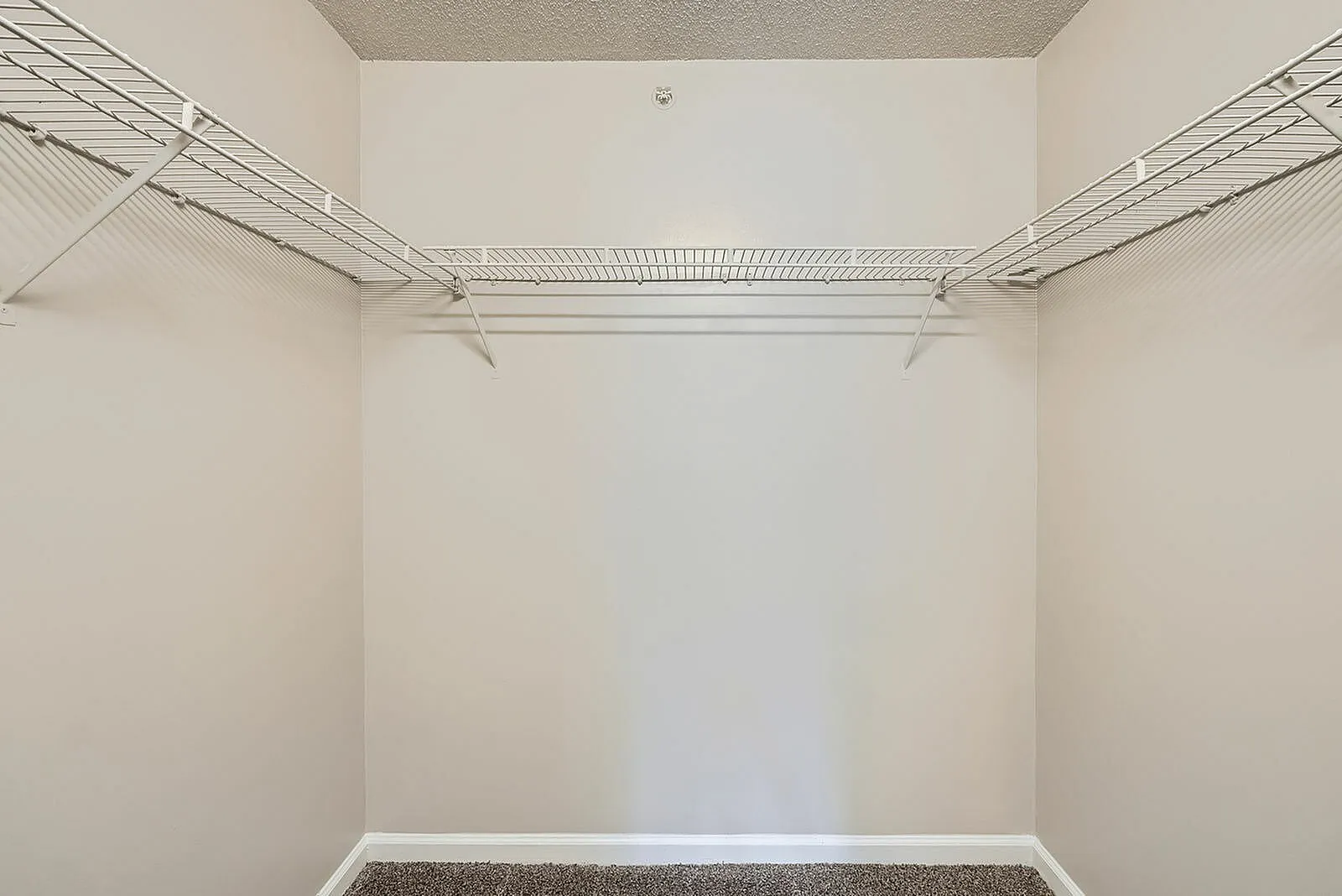 Walk-in closet, wire shelving, carpet flooring, white walls, bright lighting