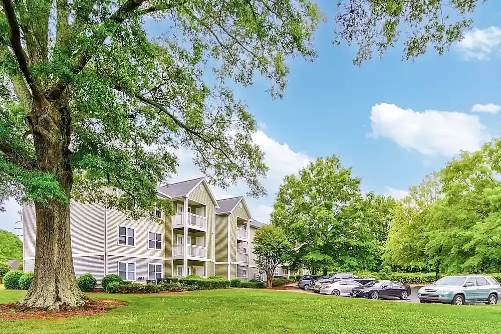 Multi-story apartment building, mature trees, manicured lawn, parked cars