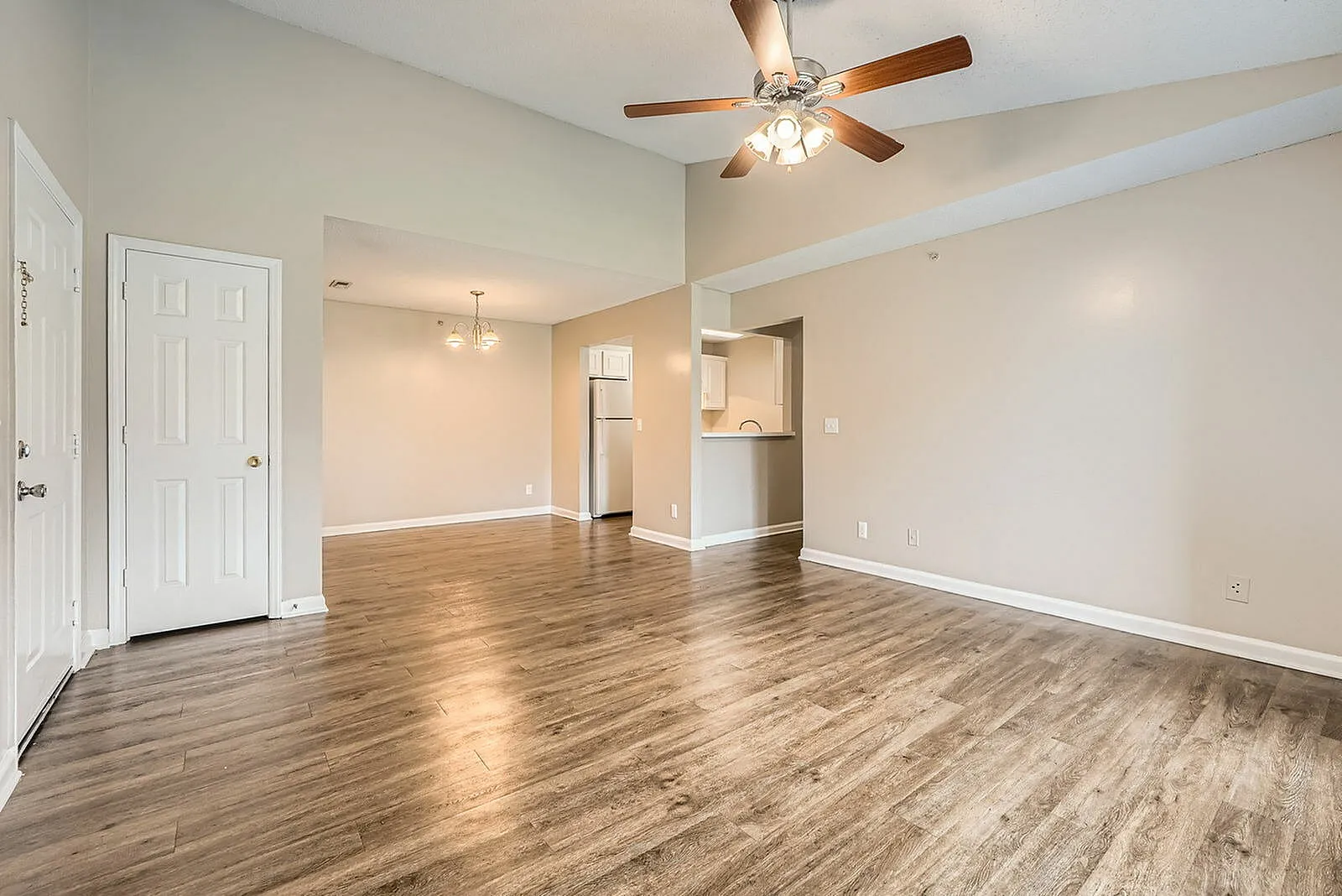 Living room, wood-style plank flooring, ceiling fan, white trim, open kitchen view