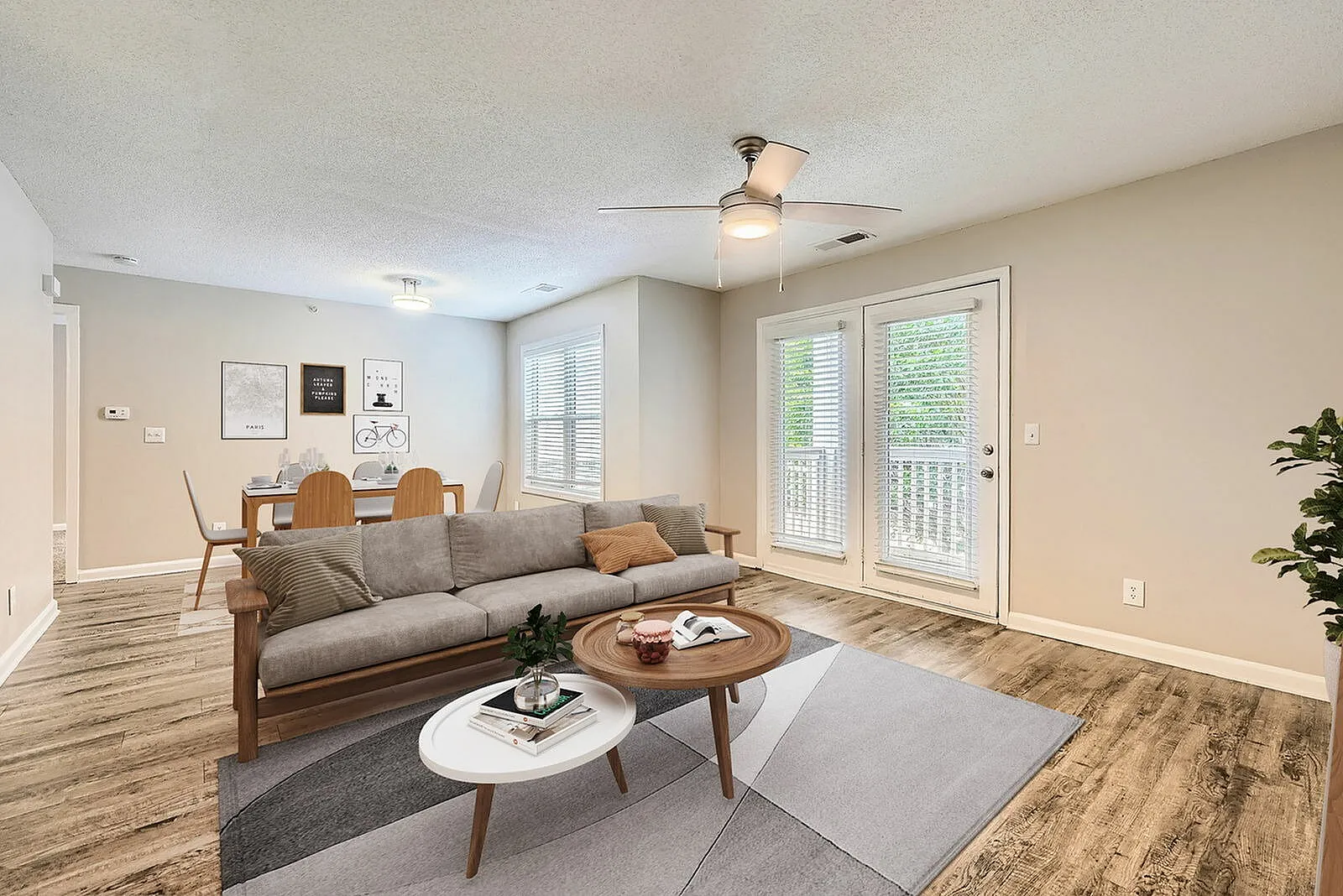 Living room, wood-style plank flooring, gray upholstered sofa, wood coffee tables, ceiling fan, glass patio doors