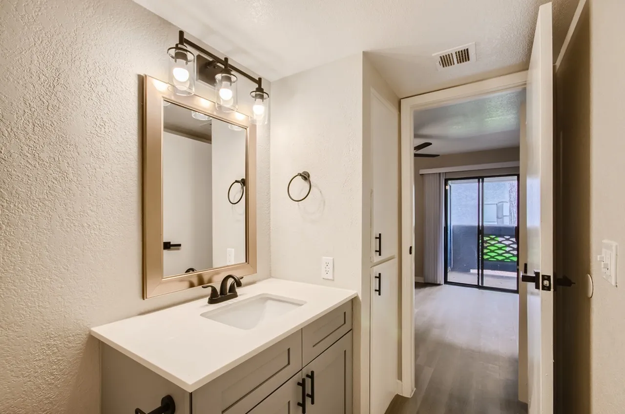 Primary bathroom vanity, framed mirror, vanity light fixture, white countertop, bedroom view beyond