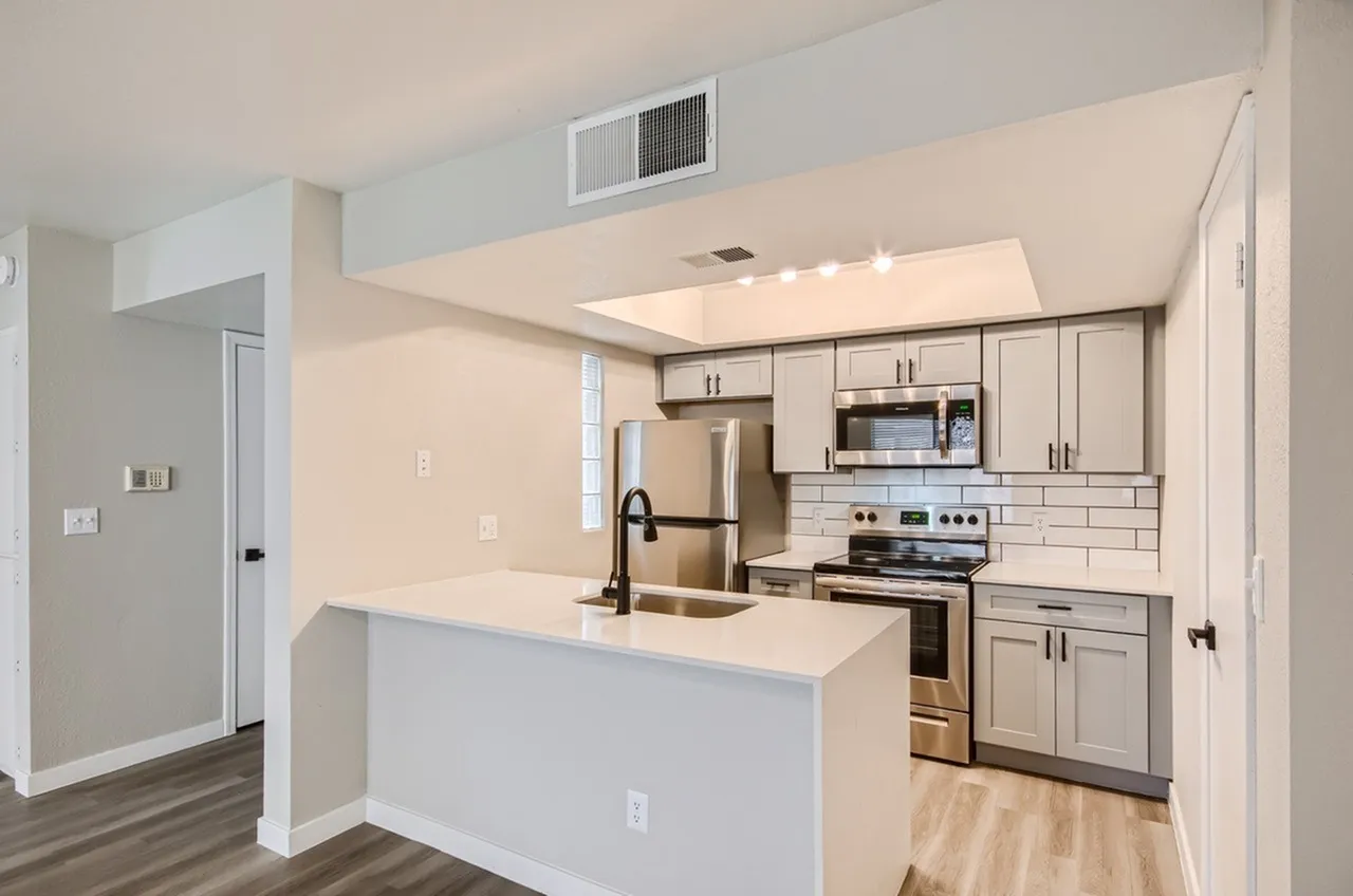 Kitchen, white peninsula countertop, gray cabinetry, stainless steel appliances, black faucet, recessed ceiling detail