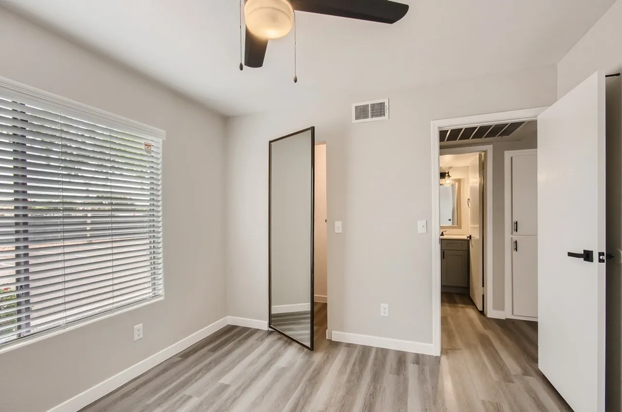 Bedroom, window with horizontal blinds, wood-style plank flooring, lookout to hallway bathroom