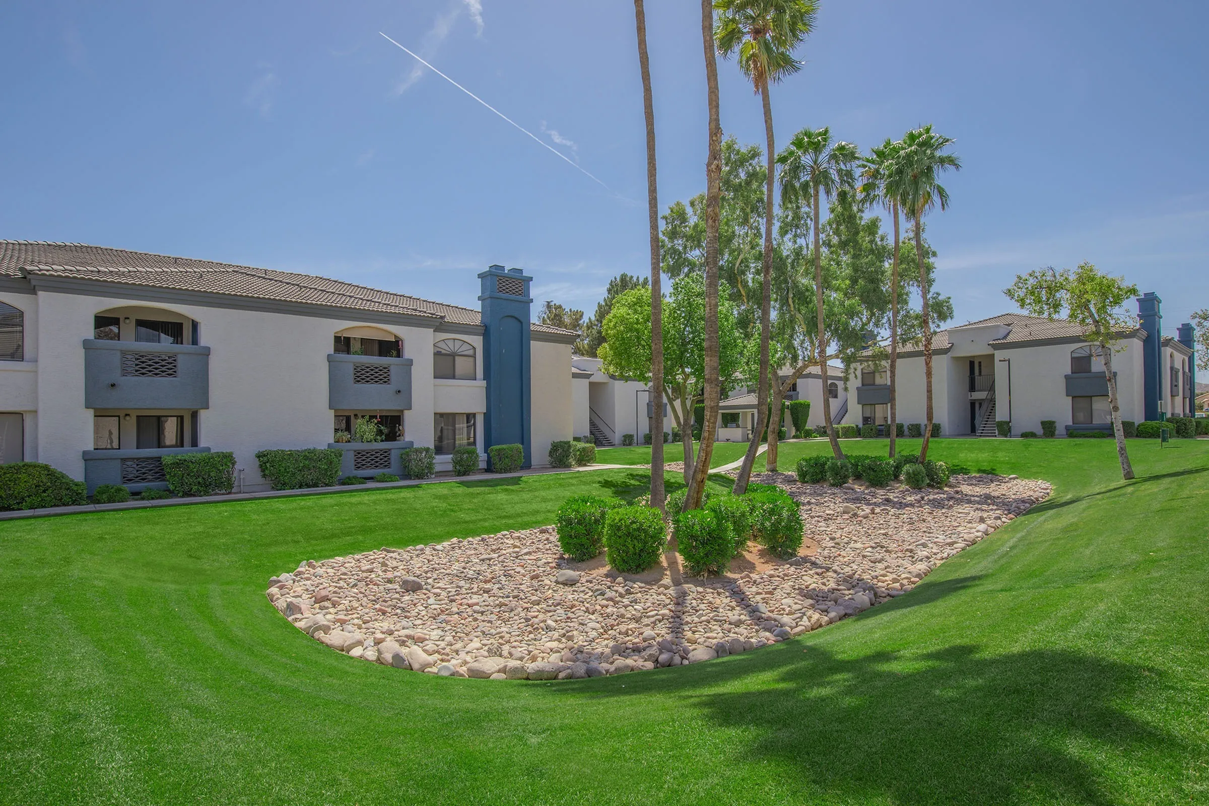 Landscaped courtyard, green lawn, desert rock accent, palm trees, apartment buildings